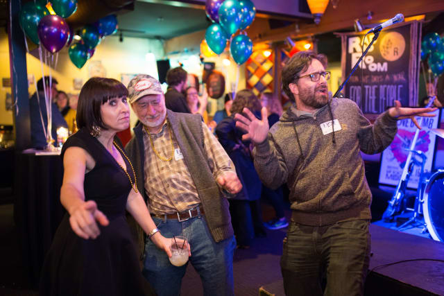 Guests enjoying the Love Bomb 2017 event, dancing and socializing, with colorful balloons and a microphone setup in the background.